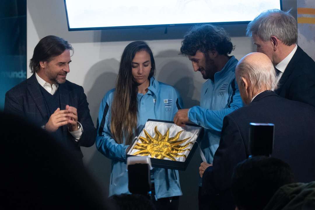 La velerista Dolores Moreira (2-i) y el jugador de rugby Diego Ardao (3-d) fueron registrados este martes, 9 de julio, al recibir la bandera de Uruguay, de manos del presidente del país, Luis Lacalle Pou (i), del secretario nacional de Deporte, Sebastián Bauza (d), y del presidente del Comité Olímpico de Uruguay, Julio Cesar Maglione (2d), durante la despedida a la delegación de deportistas que representarán al país sudamericano en los Juegos Olímpicos de París 2024, en Montevideo (Uruguay). EFE/Sofía Torres